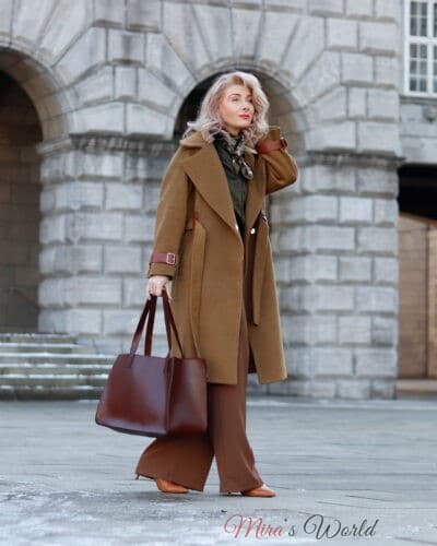 Frau im eleganten Mantel mit Handtasche im Freien.