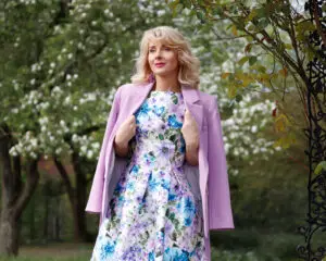 Woman in floral dress and pink coat outdoors.