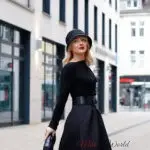 Woman in stylish hat and black outfit outdoors.