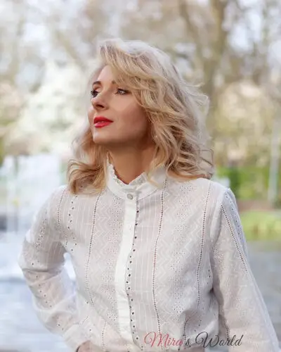 Woman in white blouse looking upwards outdoors.