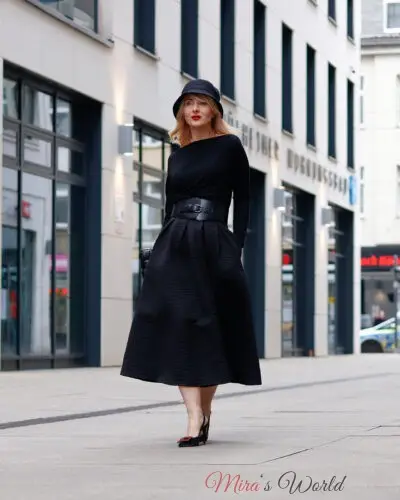 Woman in chic black outfit and hat outdoors.