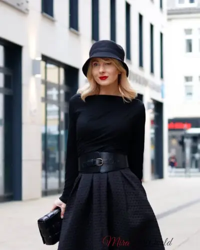 Woman in chic black outfit and hat outdoors.